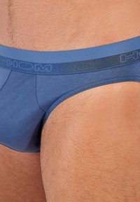 Modré pánské slipy vyrobené z měkkého materiálu s širokým modrým elastickým pasem, na kterém se nachází logo "HOM" v kontrastním provedení.