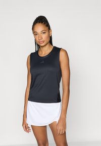 Μαύρο αθλητικό τοπ χωρίς μανίκια με στρογγυλή λαιμόκοψη και ριμπ υφή, συνδυασμένο με λευκή φούστα με διακριτικό σχέδιο και πλαϊνή σχισμή.