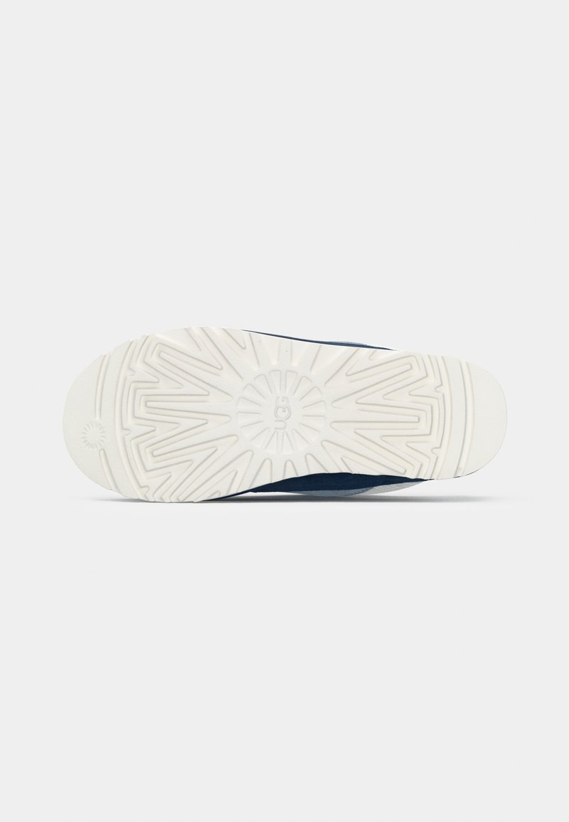 Suela de zapato con una parte inferior de goma blanca texturizada, que presenta un diseño geométrico y una marca grabada en el centro.