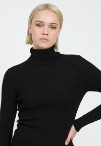 Schwarzer gerippter Rollkragenpullover, taillierte Passform mit langen Ärmeln, aus strukturiertem Strickstoff hergestellt. Glatte Oberfläche und hoher Kragen.