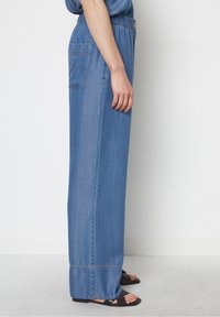 Ljusblå jeans med vida ben, elastisk midja och en bakficka. Detaljerad sömnad vid fållen.