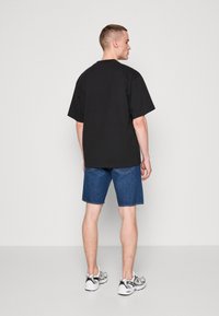 Tricou negru supradimensionat, cu mâneci scurte, purtat împreună cu pantaloni scurți din denim albastru, până la genunchi. O pereche de adidași albi și argintii completează ținuta.