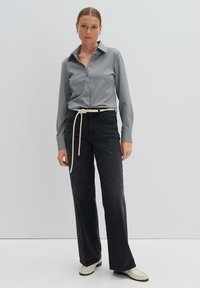 Grau gestreiftes Hemd mit langen Ärmeln, kombiniert mit schwarzen weit geschnittenen Hosen und einem beige-farbenen Gürtel. Die Schuhe sind cremefarbene Mokassins.