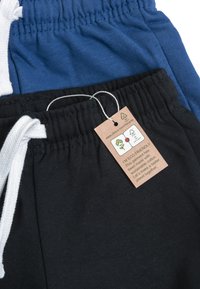 Två par bomullsmjukisbyxor: ett par blå med vita dragsnören, ett par svarta med en etikett som anger miljövänliga material. Bekväm passform, elastisk midja.