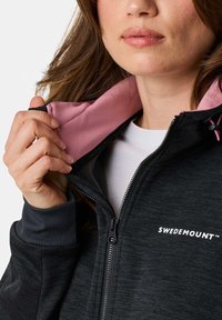 Black zip-up hoodie with pink inner lining; features a logo on the chest, ribbed cuffs, and a smooth texture. Zipper is black.