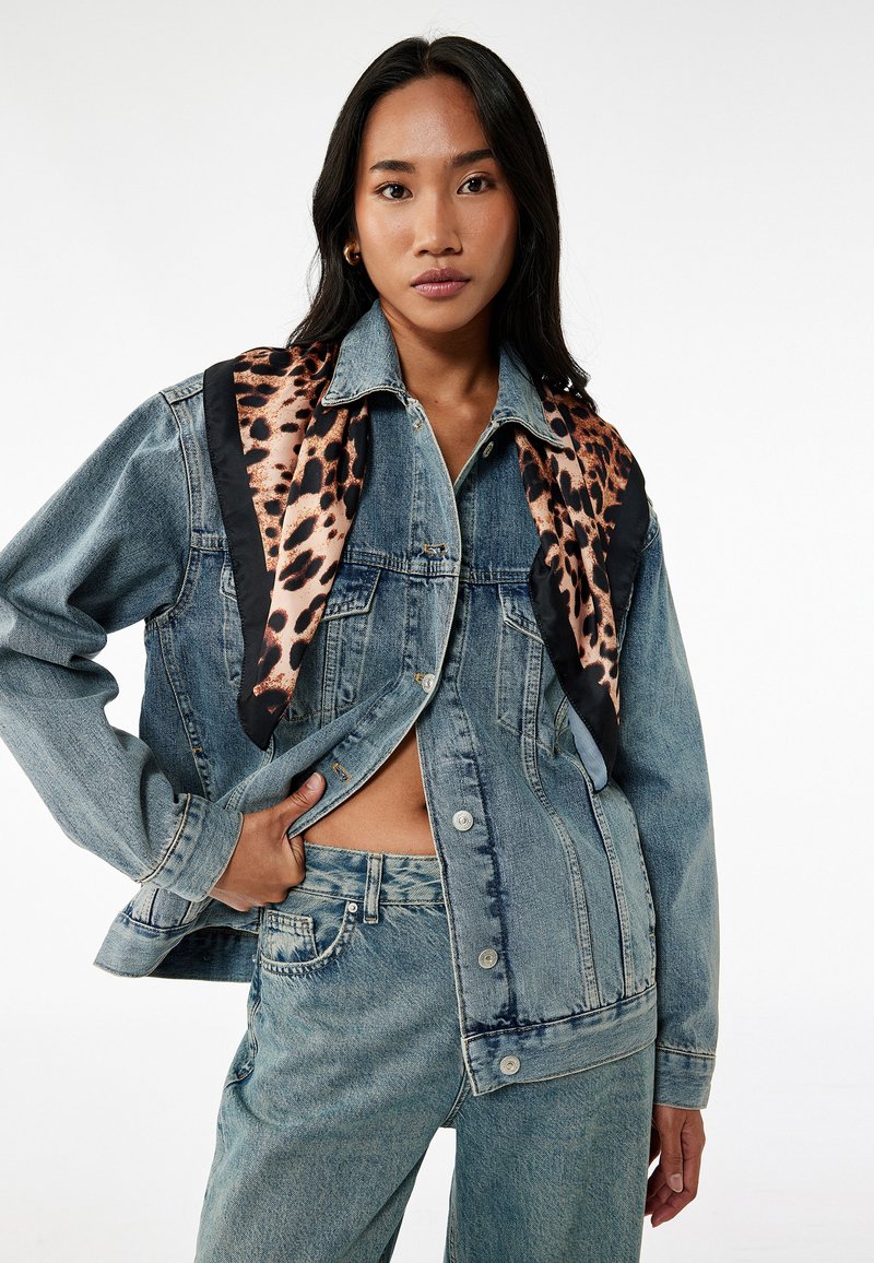Chaqueta de mezclilla con un acabado azul desgastado, que presenta mangas largas, cierre de botones y una bufanda con estampado de leopardo drapeada alrededor del cuello.