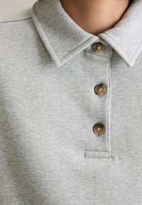Gray polo shirt with a textured fabric, featuring a pointed collar and three brown buttons down the front, and a small chest opening.