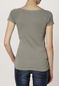 Šedé tričko s krátkým rukávem a krajkovým výstřihem ve vlnkách. Měkký, přiléhavý materiál a jednoduchý design. Nosi se s modrými džíny.