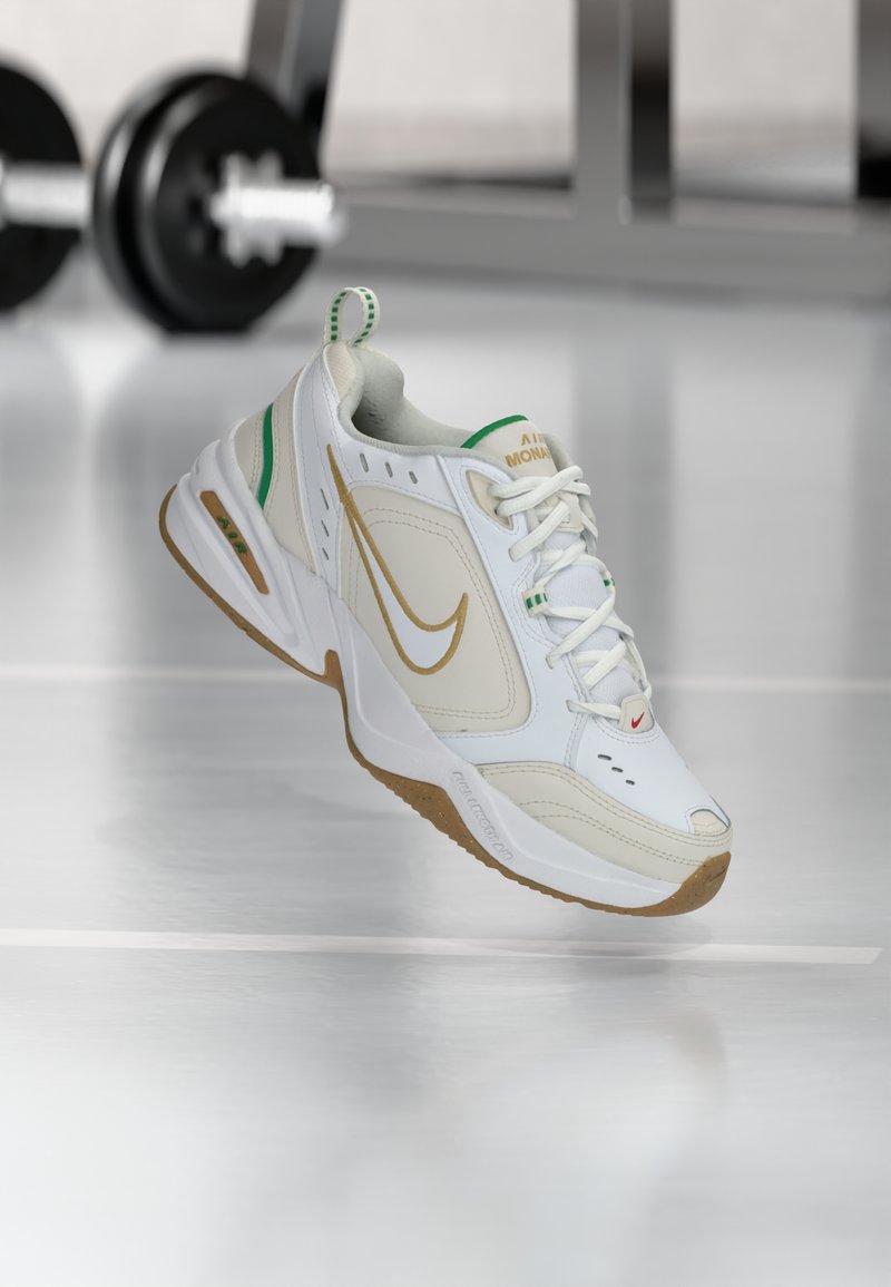 Witte sportschoen met een leren bovenwerk met textuur, gouden Nike swoosh, groene accenten en een gumkleurige zool. Voorzien van vetersluiting en een gewatteerde kraag.
