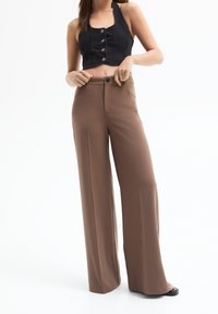 Zkrácený černý denimový top se zapínáním na knoflíky, doplněný širokými hnědými kalhotami. Oba kusy mají hladkou texturu a střih na míru.