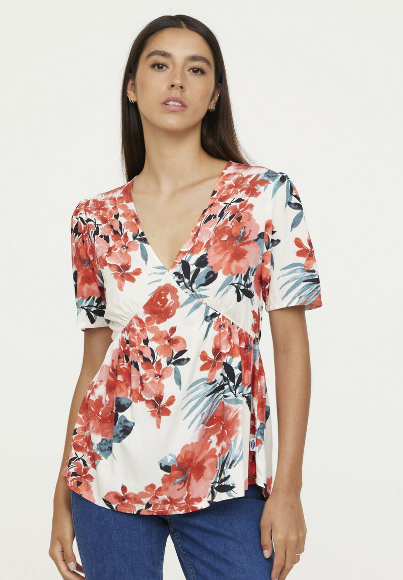 Haut fleuri avec un décolleté en V profond, des manches courtes et une taille cintrée. Présente des motifs floraux rouges et bleus sur un fond blanc.