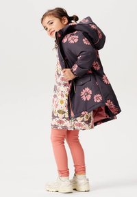 Svart och rosa blommig puffjakka med ett mönstrat innerfoder, tillsammans med rosa ribbade leggings och beige sneakers.