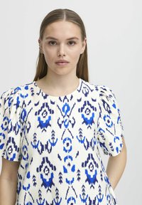 Top bianco con motivi astratti blu e navy, caratterizzato da maniche a sbuffo e scollatura rotonda. Tessuto liscio in un materiale leggero.
