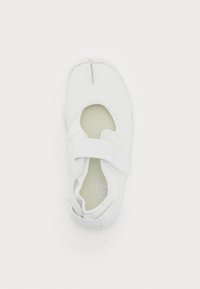 White athletic shoe with a smooth, textured upper, elastic strap, and rounded toe. Features a mesh lining and solid rubber sole.