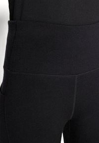 Sorte leggings laget av glatt, stretchy stoff med høy midje og flate sømmer. Ingen synlige mønstre eller maskinvarer.