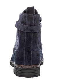 Marineblauwe suède enkellaars met een gestructureerd paneel, achterrits en rubberen zool. Kenmerkt zich door een wikkelband rond de enkel.