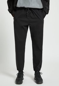 Svarta joggarbyxor tillverkade av lättviktigt tyg, med elastisk midja och snörning, avslutade vid anklarna och sidofickor.