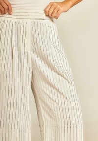 Witte wijde broek met verticale metallic strepen. De stof is soepel met een op maat gemaakte hoge tailleband en geplooide voorzijde.