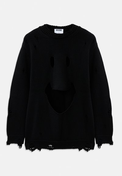 Pull en tricot noir avec des trous usés formant un visage souriant sur le devant et de petites déchirures éparpillées à travers le tissu.