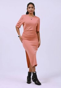 Ροζ μεσαίο φόρεμα με κοντά μανίκια, εφαρμοστή μέση και πλαϊνή σχισμή, συνδυασμένο με μαύρα μποτάκια αστραγάλου με αγκράφες. Λείο ύφασμα.