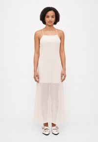 Lys beige ermeløs kjole med en paljettdekket overflate, lang gjennomsiktig overdel og teksturerte leggings under. Brukt med hvite slip-on sko.