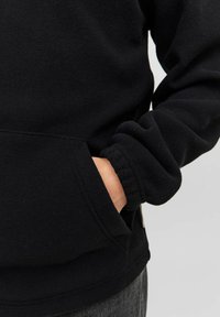 Pulóver de forro polar negro con un bolsillo tipo canguro, puños acanalados y textura suave. El material parece cálido y cómodo.