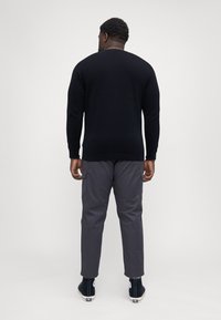 Pulover negru din tricot, pantaloni cargo gri și adidași negri cu guler înalt. Puloverul are guler rotund; pantalonii au buzunare laterale și o croială relaxată.