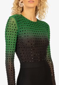 Langdurige jurk met een verloop van groen naar zwart, versierd met vierkante studs. Gladde textuur met een aansluitende zwarte rok.