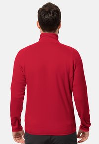 Veste rouge à manches longues avec un col montant ; tissu lisse et extensible ; design ajusté ; minimaliste sans logos ou motifs visibles.