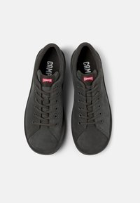 Sneaker in suede nero con design low-top, punta rotonda e allacciatura frontale. Presenta un'etichetta rossa con logo sulla linguetta e suola in gomma testurizzata.