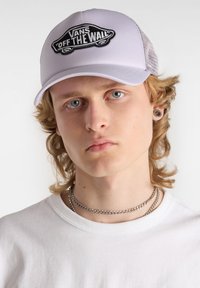 Gorra snapback blanca de malla con un logo bordado en negro de "Vans 'Off the Wall'" en la parte frontal. Cuenta con un visera curva y ajuste ajustable.