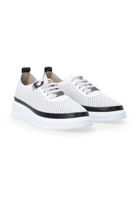 Białe perforowane sneakersy z czarnymi akcentami, okrągły нос, wyściełany kołnierz i gruba biała podeszwa. Sznurowadła przeplecione przez oczka dla pewnego dopasowania.