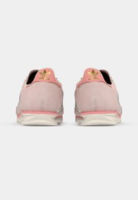 Rózsaszín velúr sportcipő fehér középtalppal, arany logóval a hátulján és világos rózsaszín díszítésekkel. Kerekített forma, texturált felső résszel.