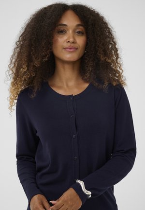 Tmavomodrý pletený kardigán s okrúhlym výstrihom, zapínaním na gombíky vpredu a dlhými rukávmi. Má hladkú textúru a jemný strih.