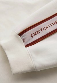 Biała koszula z długim rękawem charakteryzuje się teksturowanym materiałem oraz bordowym akcentem w paski z napisem "performance" w jasnym kolorze na rękawie.