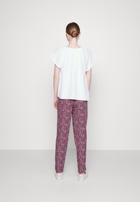 Biała bluzka z krótkim rękawem o teksturowanej tkaninie zestawiona z różowymi spodniami w wzory. Strój charakteryzuje się luźnym krojem i minimalnymi detalami.