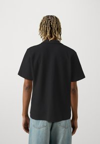 Must have tekstuuriga must lühikeste varrukatega särk, millel on krae ja lõdvem istuvus, koos helesiniste teksashortsidega.