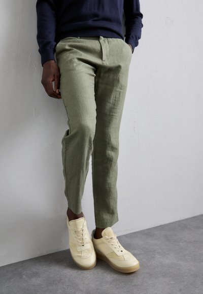 Lichtgroene linnen broek met een rechte snit, gecombineerd met off-white sneakers met een gladde textuur en subtiele accenten.