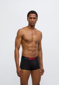 Μαύρα μποξεράκια κατασκευασμένα από απαλό ύφασμα, με κόκκινη μέση που φέρει το λογότυπο «DIESEL». Ο σχεδιασμός έχει στενή εφαρμογή και μινιμαλιστικό στυλ.