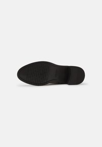 Suela de zapato negra con patrón texturizado y nombre de marca en relieve. Forma redondeada, leve tacón, con un acabado mate suave.