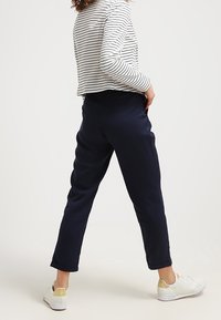 Pantalons bleu marine à coupe décontractée avec une texture lisse, ourlés au niveau de la cheville, associés à un haut à manches longues rayé et des baskets blanches.