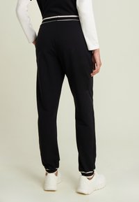 Pantalones jogger negros con un ajuste entallado, con una franja blanca en la cintura y los puños. Hechos de una tela suave, combinados con zapatillas blancas.