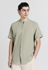 Kurzärmliges, hellgrünes Hemd mit strukturierter Oberfläche, Stehkragen und Knopfleiste vorne. Verfügt über einen abgerundeten Saum und eine lockere Passform.