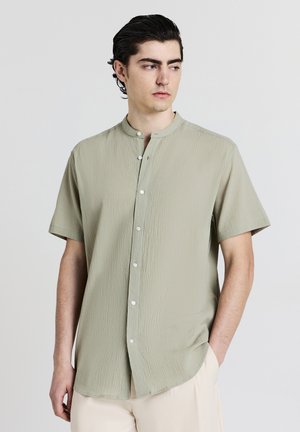 Camicia a maniche corte, verde chiaro, con una superficie testurizzata, colletto rialzato e bottoni frontali. Presenta un orlo arrotondato e una vestibilità rilassata.