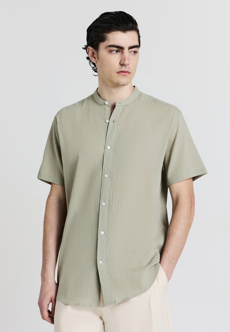 Kurzärmliges, hellgrünes Hemd mit strukturierter Oberfläche, Stehkragen und Knopfleiste vorne. Verfügt über einen abgerundeten Saum und eine lockere Passform.