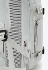 Mochila gris con un panel lateral de malla, múltiples cremalleras, correas ajustables y costuras en contraste para mayor detalle y funcionalidad.