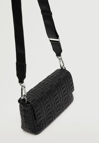 Bolso cruzado sintético negro con textura acolchada, forma rectangular, correa ajustable y acentos de hardware en plata.