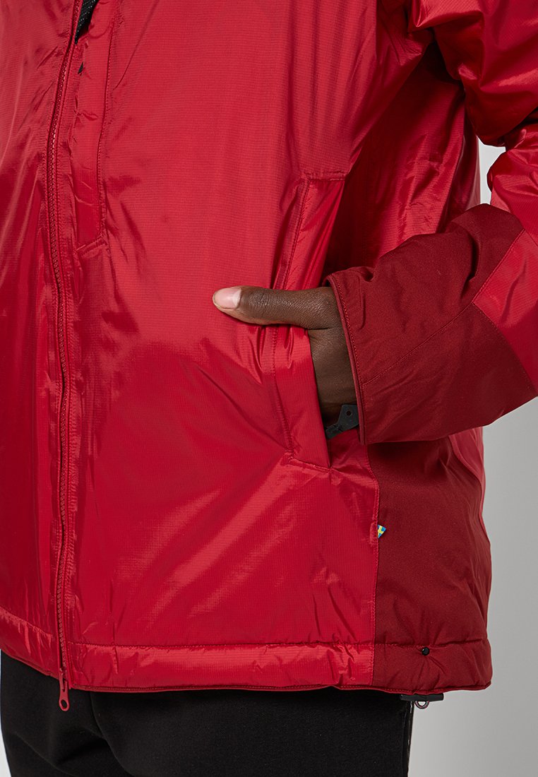 Röd isolerad jacka med en slät, blank yta, zip-förslutning framtill och sidofickor. Har kontrasterande ärmdetaljer och justerbar nederkant.