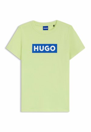 Jasnozielona koszulka z krótkim rękawem i okrągłym dekoltem, z niebieskim prostokątnym logo z napisem "HUGO" białymi dużymi literami na piersi.