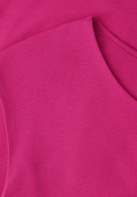 Gros plan sur un tissu tricoté rose vif avec des coutures visibles le long d'un bord replié.